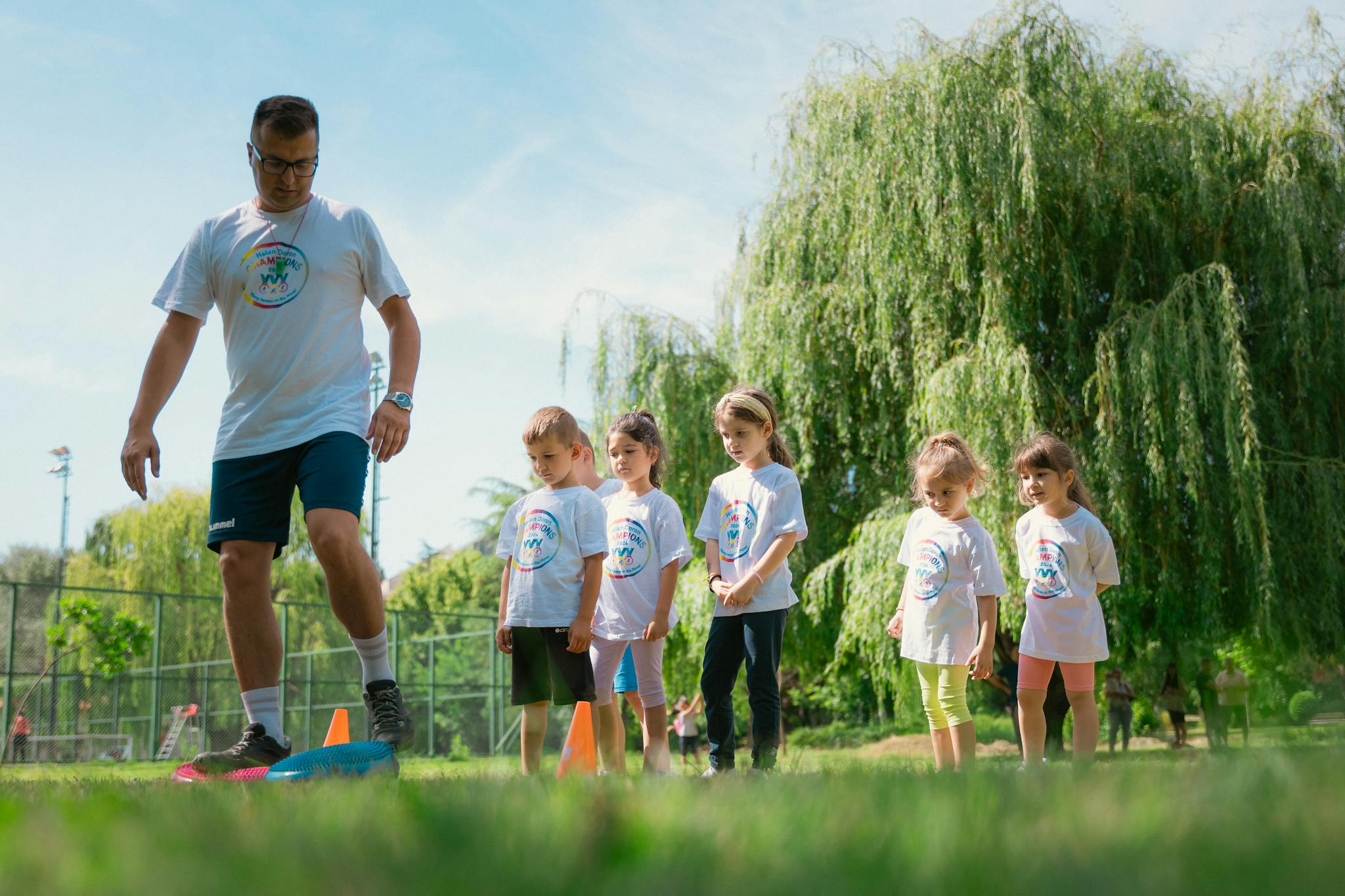 Children in a park learning sports with a coach on a sunny day.