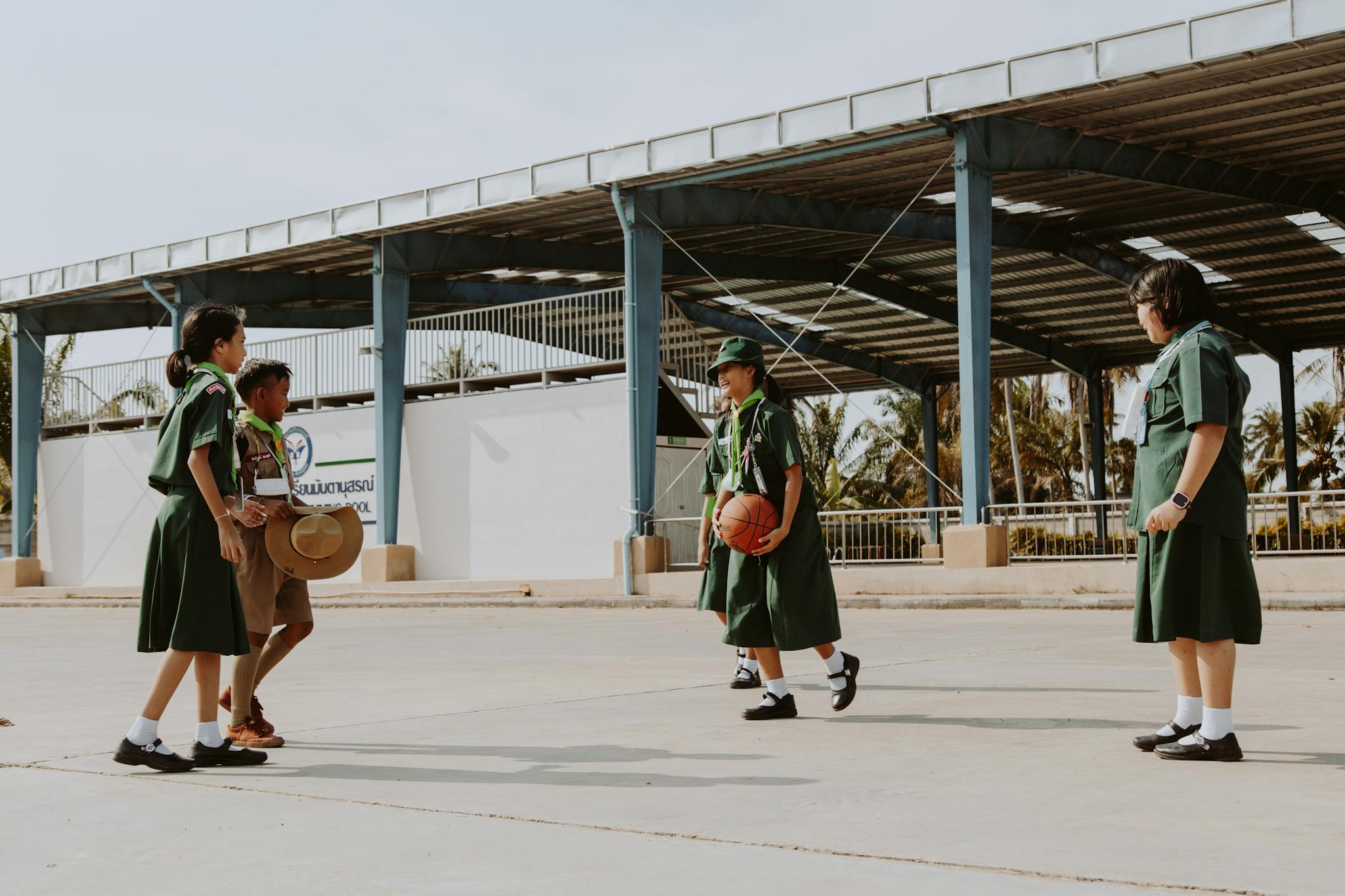 Group of students in uniforms playing basketball outdoors in a school setting.